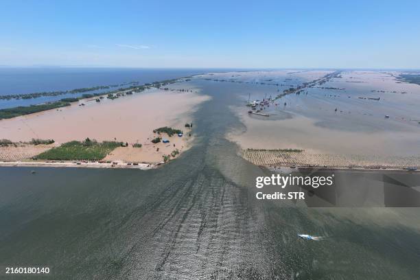 Water flows through a breach in the embankment on the shore of Dongting lake in Huarong county, in China's central Hunan province on July 6, 2024....