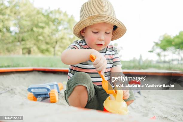 child in a straw hat playing in the sandbox in summer - sandkasten stock-fotos und bilder