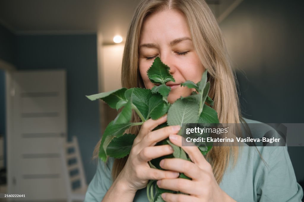 Blonde woman sniffing fresh mint at home