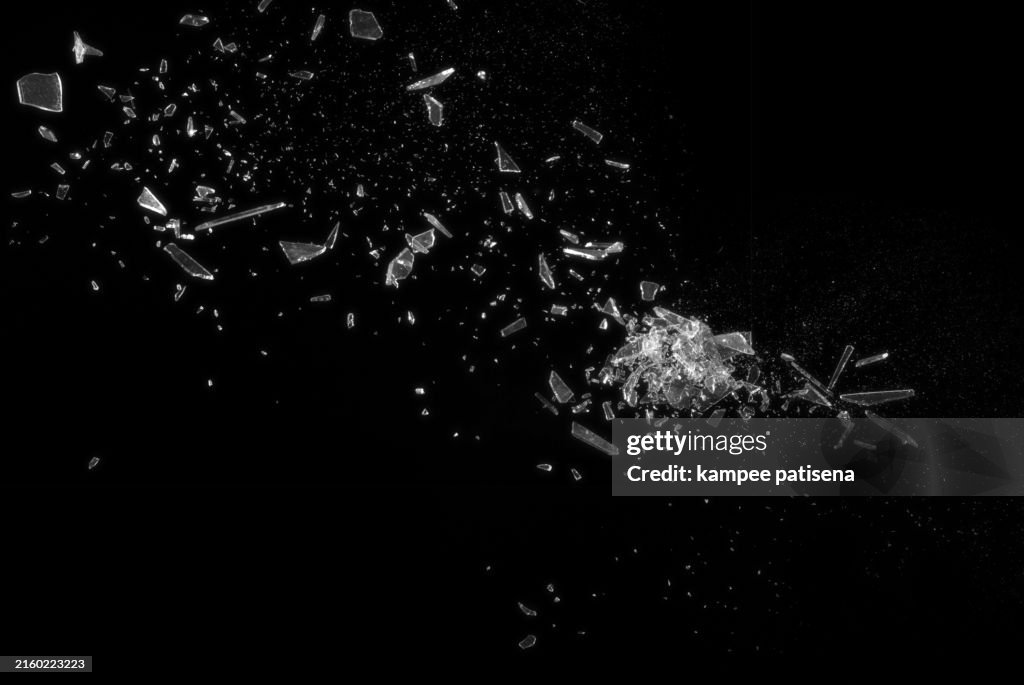 Broken Glass on Black Background shows the abstract texture of the shattered glass in great detail. The image is perfect for use in backgrounds, textures, or abstract art projects.