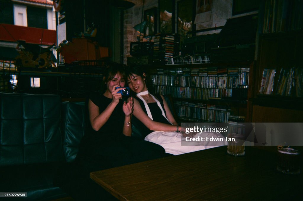 Disposable camera image of 2 asian chinese young woman looking at ccd camera screen at retro music record store cafe