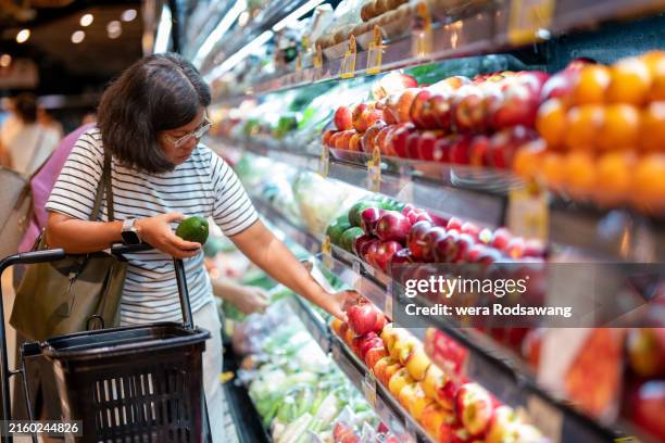 a woman choosing fresh organic fruits in aisle of a supermarket - greengrocer stock pictures, royalty-free photos & images