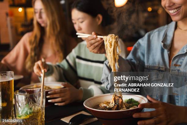 frau hebt köstliche dampfende heiße ramen-nudeln mit stäbchen - chinesische küche stock-fotos und bilder