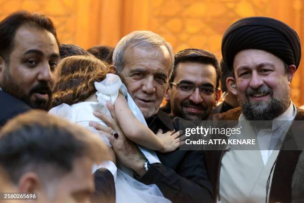 Newly-elected Iranian President Masoud Pezeshkian , is handed a child as he stands next to Hassan Khomeini, grandson of the Islamic Republic's...