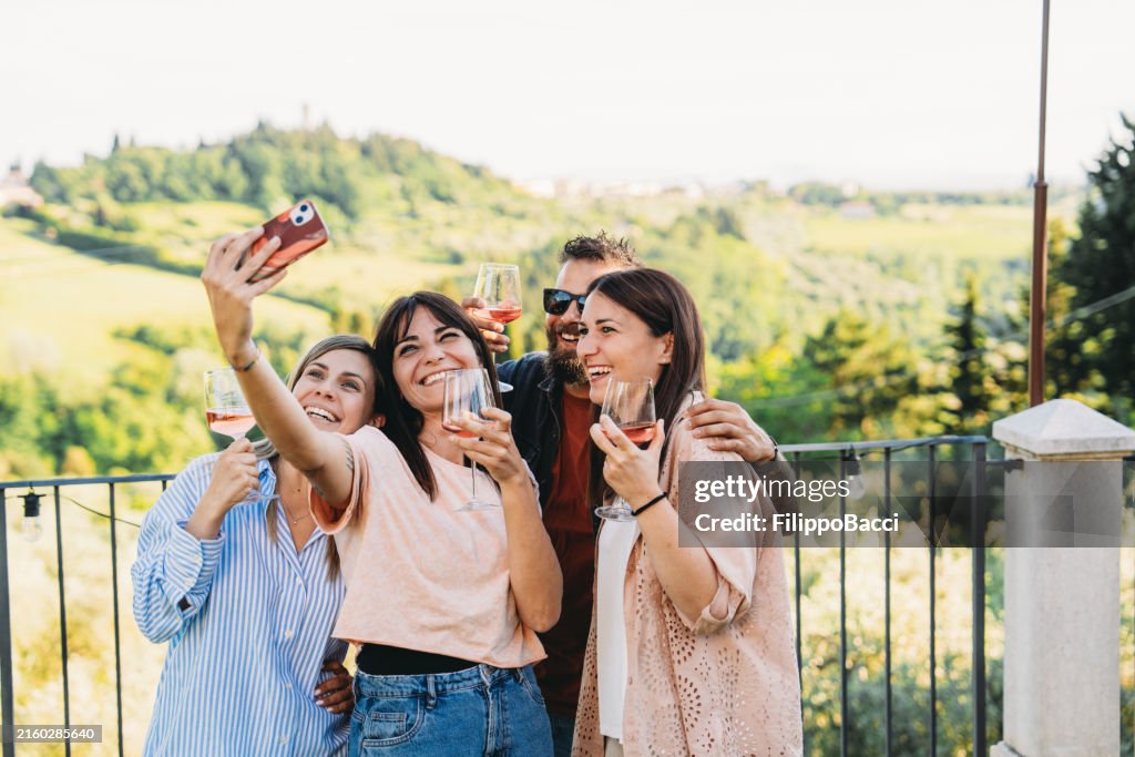 Gruppe von Freunden, die Selfie machen, während sie Wein auf dem Balkon mit Blick auf den Weinberg genießen