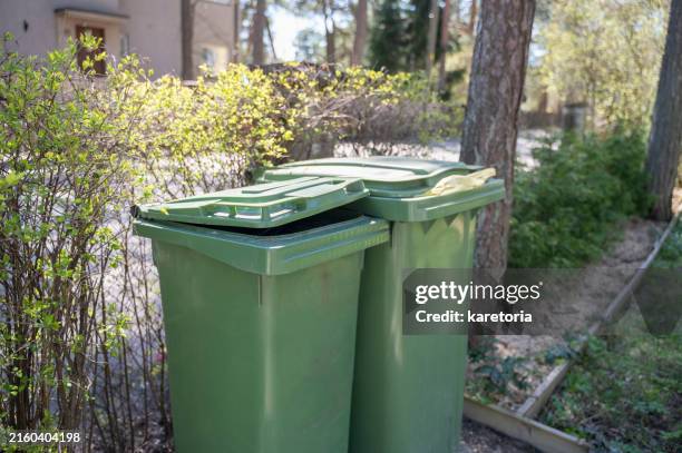 two garbage bins stand by fence of house - vuilnisbak stockfoto's en -beelden
