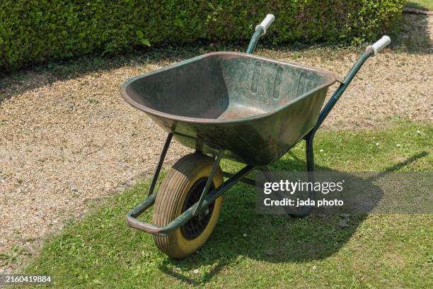 green wheelbarrow with white handles stands outside on the grass - schubkarre stock-fotos und bilder