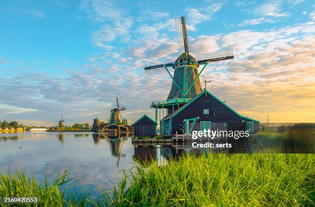 dawn's serenity: traditional dutch windmills at zaanse schans, zaandam, netherlands, amidst fishing shelters and canal boats in the early morning glow - amsterdam stock pictures, royalty-free photos & images