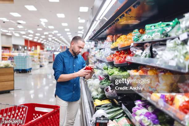 hispanic man chooses colorful bell peppers from the produce section - americana mall imagens e fotografias de stock