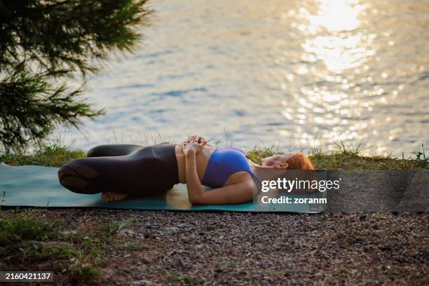 bella donna sdraiata sul tappetino sulla spiaggia isolata, che si allunga al tramonto - lentezza foto e immagini stock