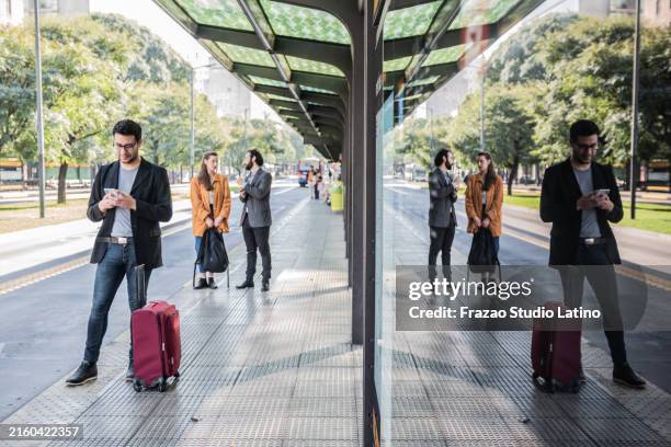 mid adult man using mobile phone on a bus stop - veículo terrestre comercial imagens e fotografias de stock