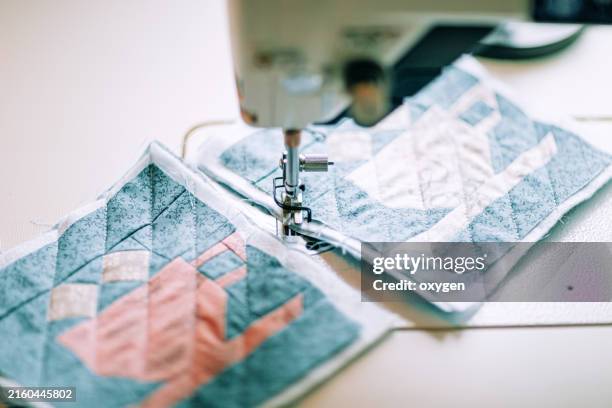 sewing machine quilting patchwork squares. close-up of a sewing machine stitching two colorful patchwork quilt squares, showcasing intricate quilting details. - patchwork stockfoto's en -beelden