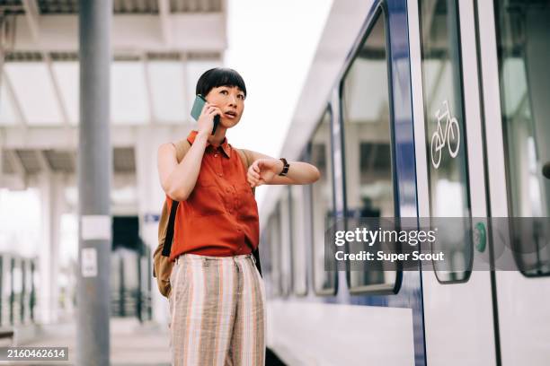 asiatische frau, die auf dem bahnsteig auf den zug wartet - auf die uhr sehen stock-fotos und bilder