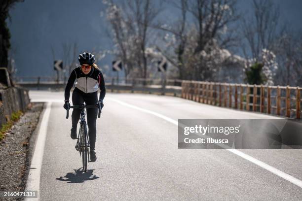 woman road cycling on italian alpine road - wielrennen stockfoto's en -beelden