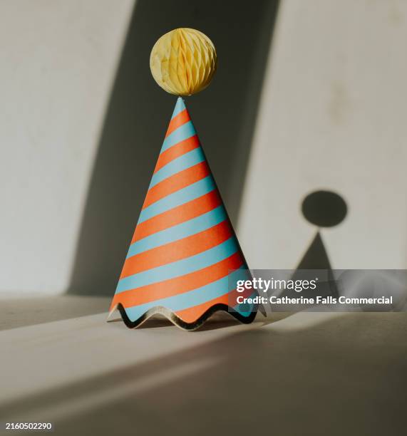 simple image of a single striped party hat casting a shadow - party hat stock pictures, royalty-free photos & images