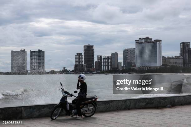 Motorbike driver sits by the seafront as unfinished buildings are seen in the background on July 1 in Sihanoukville, Cambodia. China's property...