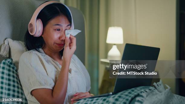 jeune fille asiatique addiction aux médias sur le lit porter un casque pleurer regarder son film préféré en streaming en ligne vod, vidéo à la demande à la maison la nuit. insomnie, cybermalgie, nomophobie, trouble du sommeil. - larme photos et images de collection