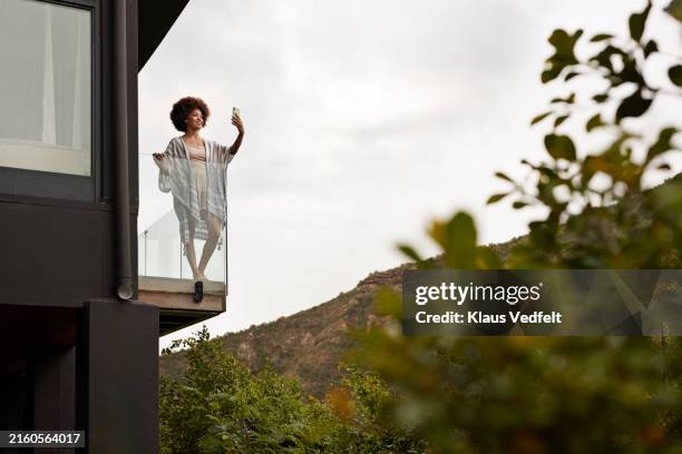 smiling young woman standing in balcony taking selfie - safari lodge stock pictures, royalty-free photos & images