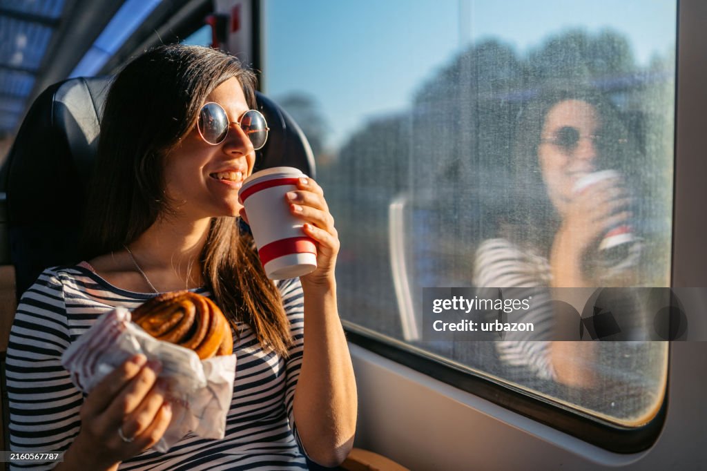 Young Woman Drinking Coffee And Eating A Bagel While Riding In A Train Through Lubeck In Germany