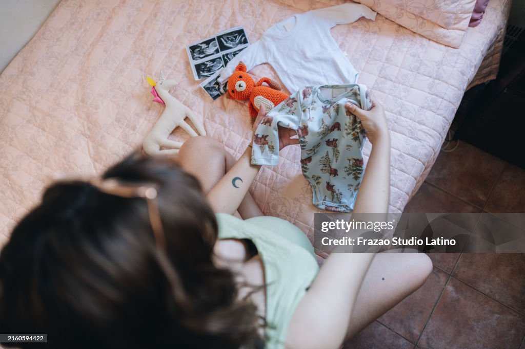 Close-up of a pregnant woman holding baby clothes in the bedroom