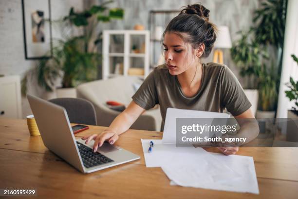 frau, die an einem laptop arbeitet, mit papieren an einem tisch. - papierkram stock-fotos und bilder