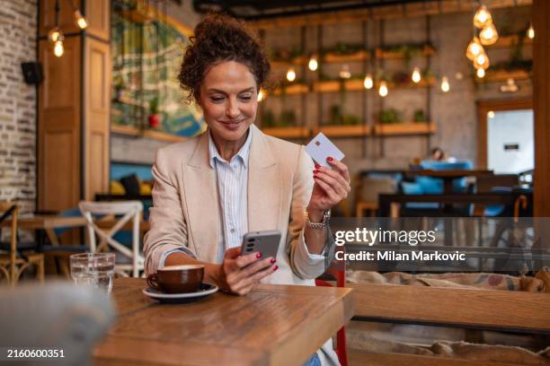 donna moderna e contemporanea seduta in caffetteria che utilizza il telefono cellulare per l'online banking o lo shopping online - biglietto foto e immagini stock