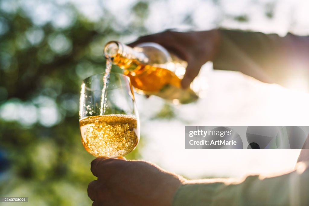 Hombre vertiendo vino blanco en un vaso en el patio trasero
