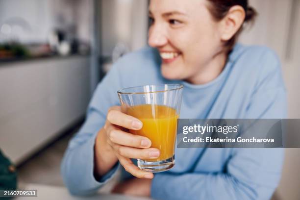 woman holding a glass of orange juice. smiling and looking away. copy space on the right. - orangensaft stock-fotos und bilder