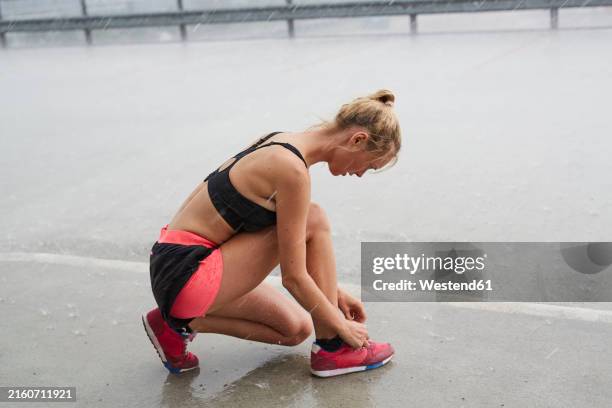 young woman tying shoe in rains on road - blonde shower stock pictures, royalty-free photos & images