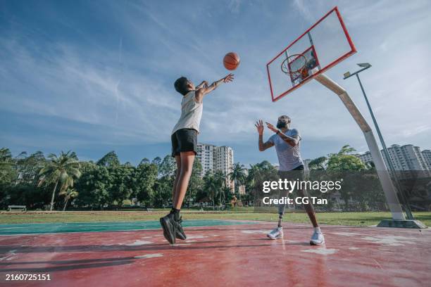 asian indian father with amputee artificial leg playing basketball with his son weekend morning - mittleres kindesalter stock-fotos und bilder