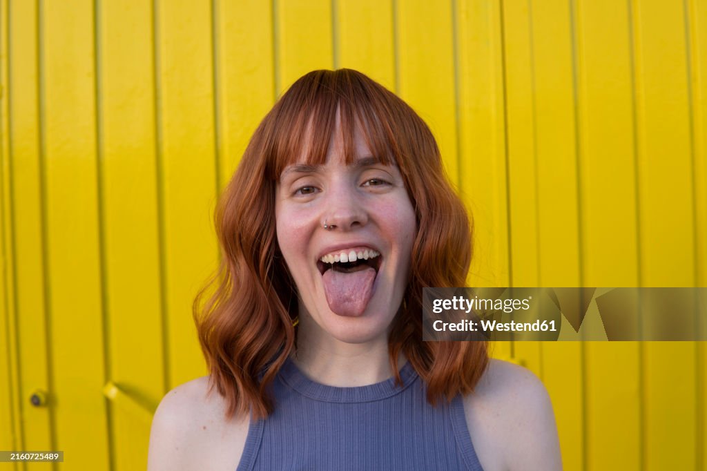 Happy redhead woman sticking tongue out in front of yellow wall
