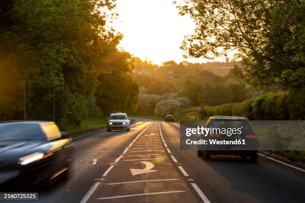 vehicles moving on country road at sunset - country road stock pictures, royalty-free photos & images