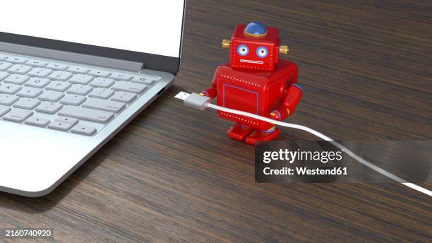 red robot with cable by laptop on table - small table stock illustrations