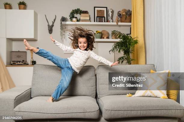 a little girl is jumping on the sofa at home - funny magic stock pictures, royalty-free photos & images