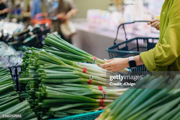 cropped shot of a young woman carrying a shopping basket, standing along the produce aisle and choosing fresh organic vegetables in a grocery store. grocery shopping. zero waste. healthy eating lifestyle and habits. sustainable and green living concept - pflanzliche ernährung stock-fotos und bilder