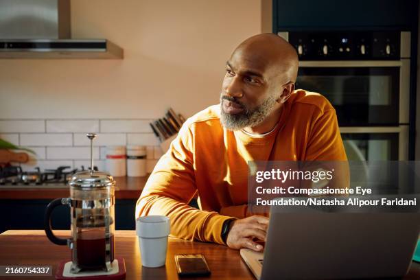 mature man using laptop at kitchen island - beschouwing stockfoto's en -beelden