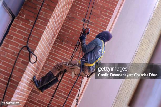bogota, colombia - a construction worker has rappelled down a building to clean repair and paint as part of routine maintenance - balaclava stock pictures, royalty-free photos & images