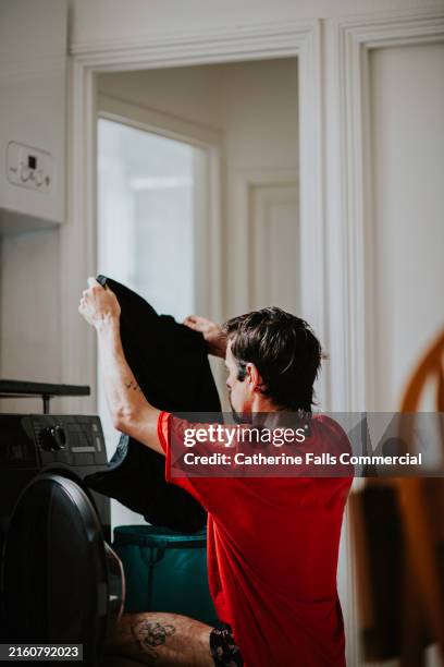 a man shakes out an item of clothing as he empties the washing machine - prueba de tinción fotografías e imágenes de stock