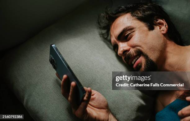 a smiling man looks at phone in bed - mensagem com foto imagens e fotografias de stock