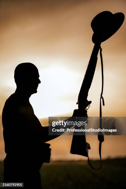hunter silhouette holding rifle and hat at sunset - sniper stock pictures, royalty-free photos & images