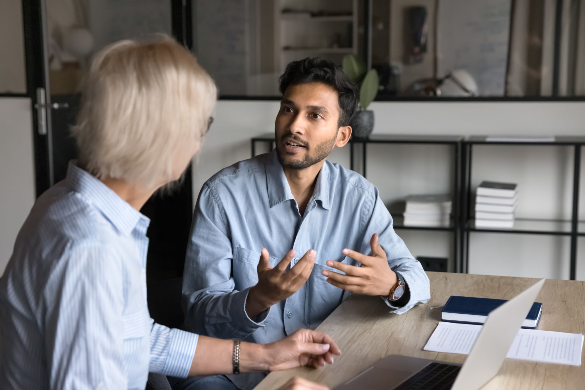 Serious younger Indian professional man talking to elder colleague woman Serious younger Indian professional man talking to elder colleague woman