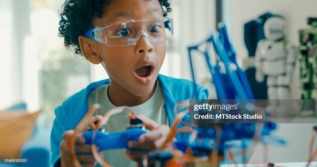 Closeup of Young African-American boy using remote control for robotics project amidst various technological tools and models at home. STEM Education robotics courses online.