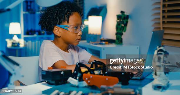 young african-american boy learning programming codes on laptop while building and programming robotics in home at night. stem education robotics courses online. - editorial stock pictures, royalty-free photos & images