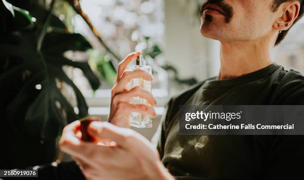 a man spritzes cologne on himself - perfume fotografías e imágenes de stock