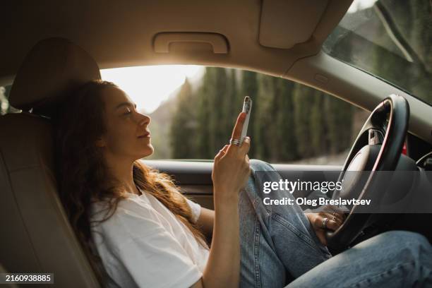 woman relaxing in car at sunset and wasting time on social media in smartphone - car instagram stock pictures, royalty-free photos & images
