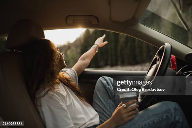 girl enjoying sunset view through car window. sitting behind the wheel with coffee - midlife crisis stock pictures, royalty-free photos & images