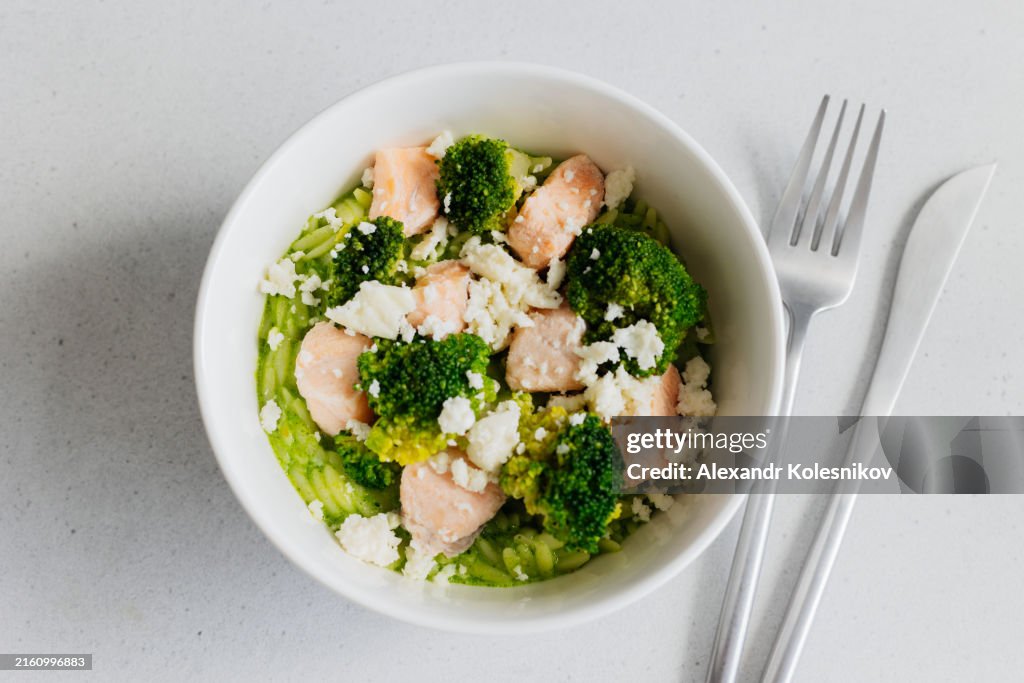 Breakfast bowl with pasta risoni, salmon fillet, broccoli and cheese on white marble background