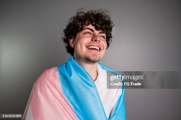 transgender male wrapped in a transgender flag contemplating on a studio shot - transgender symbol stock pictures, royalty-free photos & images