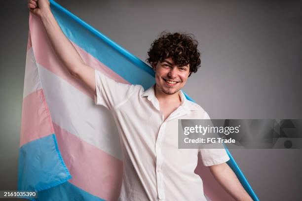 ritratto di un maschio transgender che tiene la bandiera transgender su uno scatto in studio - transgender foto e immagini stock