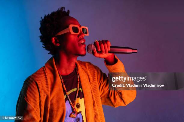 man singing into a microphone with a colored background - rapper stock pictures, royalty-free photos & images
